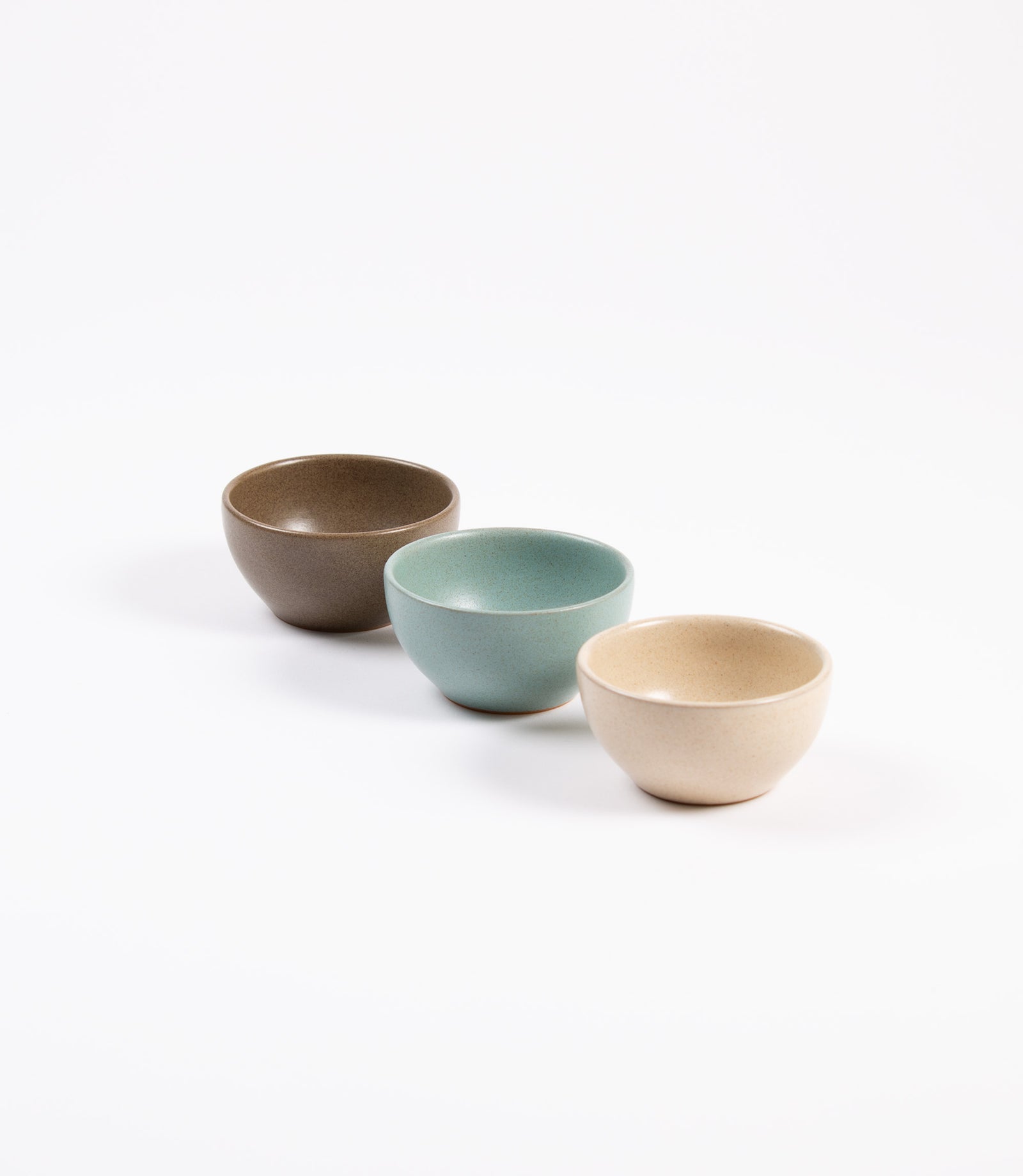 Three ceramic bowls in brown, green, and beige on a white background