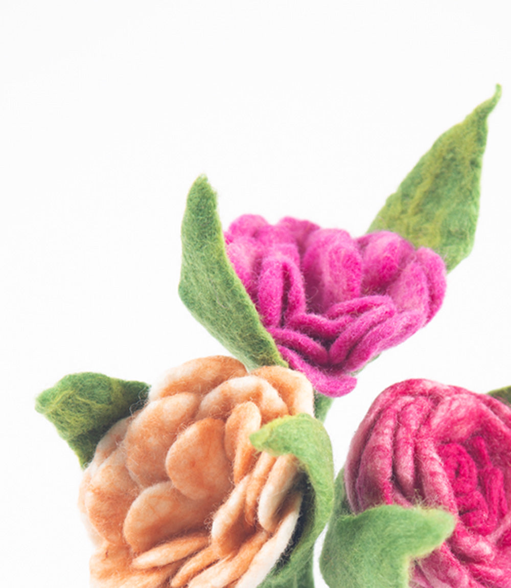 Close-up of felted flowers in pink, green, and brown on a white background