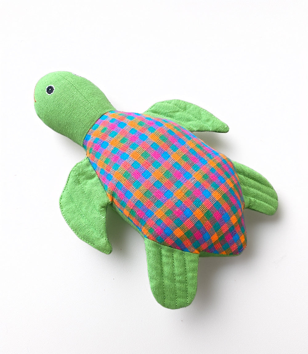 Green plush turtle toy with a colorful checkered pattern on a white background