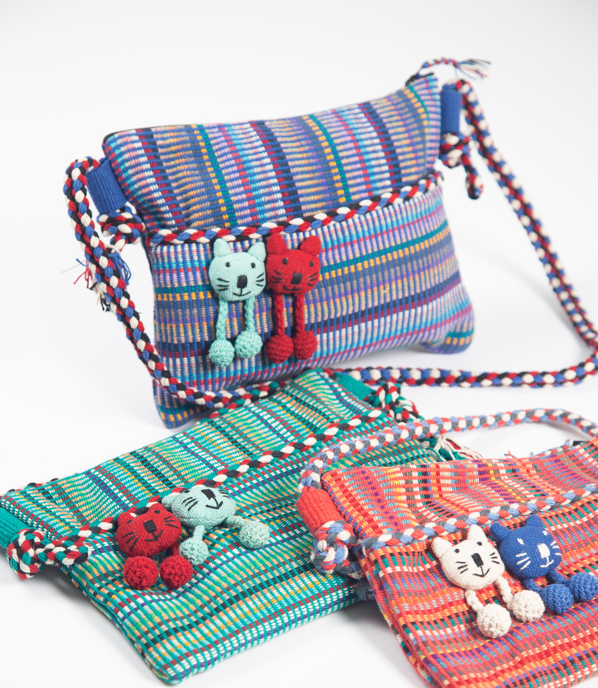 Colorful woven bags with cat-themed tassels on a white background