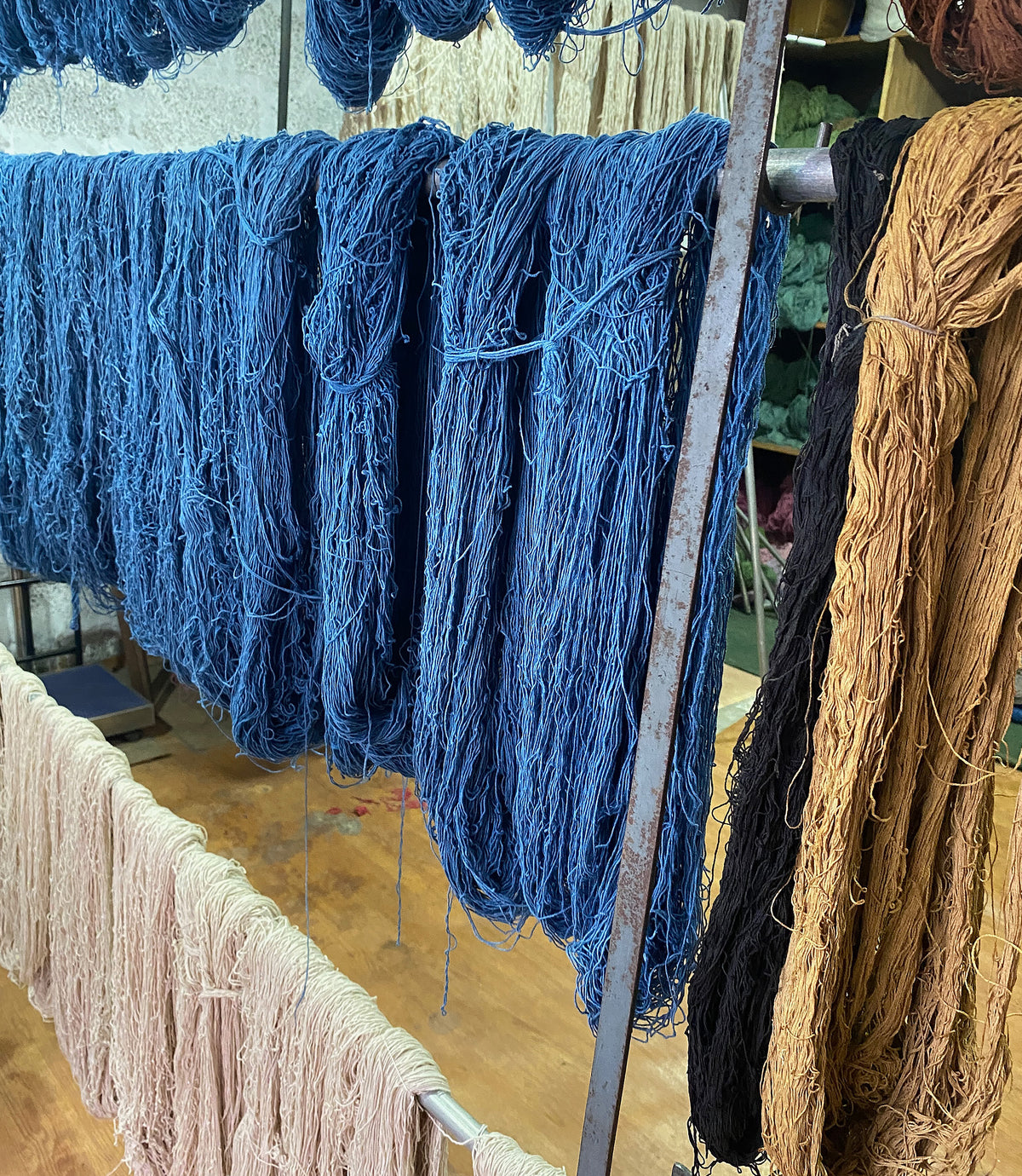 Yarns in various colors hanging on a rack, including blue, brown, and beige.