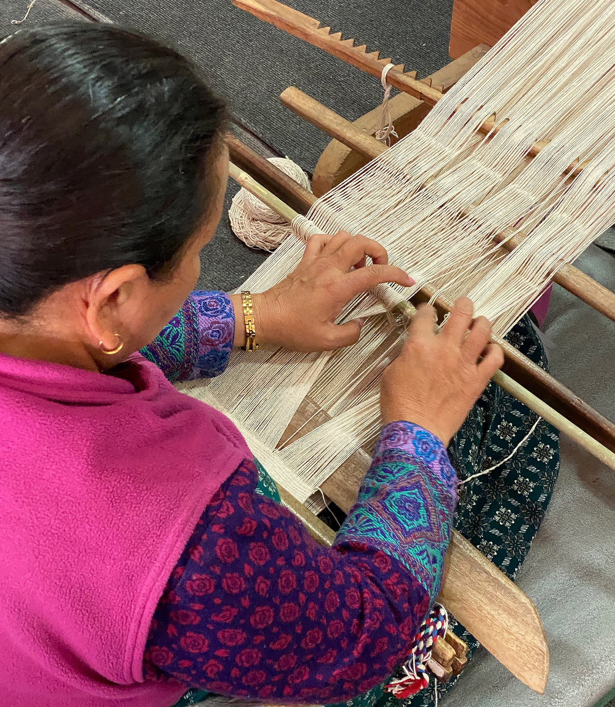 Woman weaving on a traditional loom with a focus on her hands and the fabric.