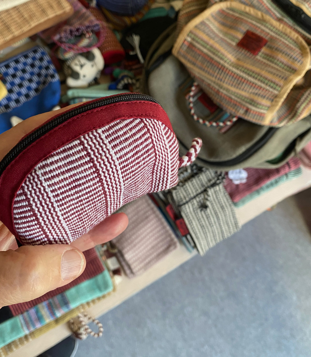 Hand holding a red and white textured pouch with a background of various other pouches.