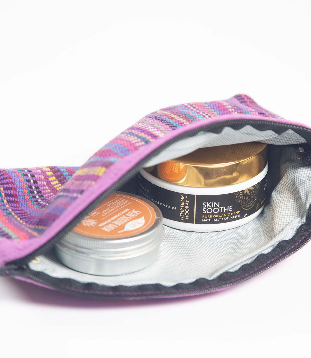 Open purple lined makeup bag with skincare products on a white background