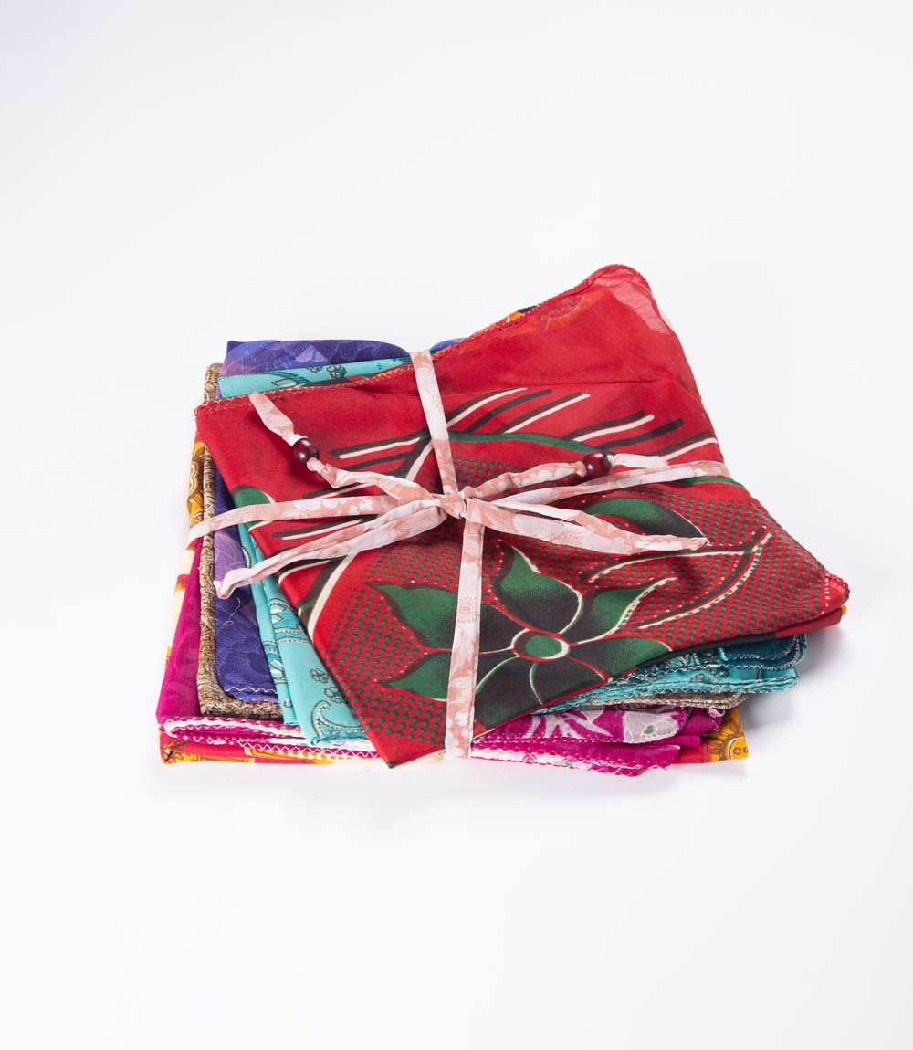 A collection of assorted colorful sari fabric gift wraps tied with a ribbon, displayed on a white background.