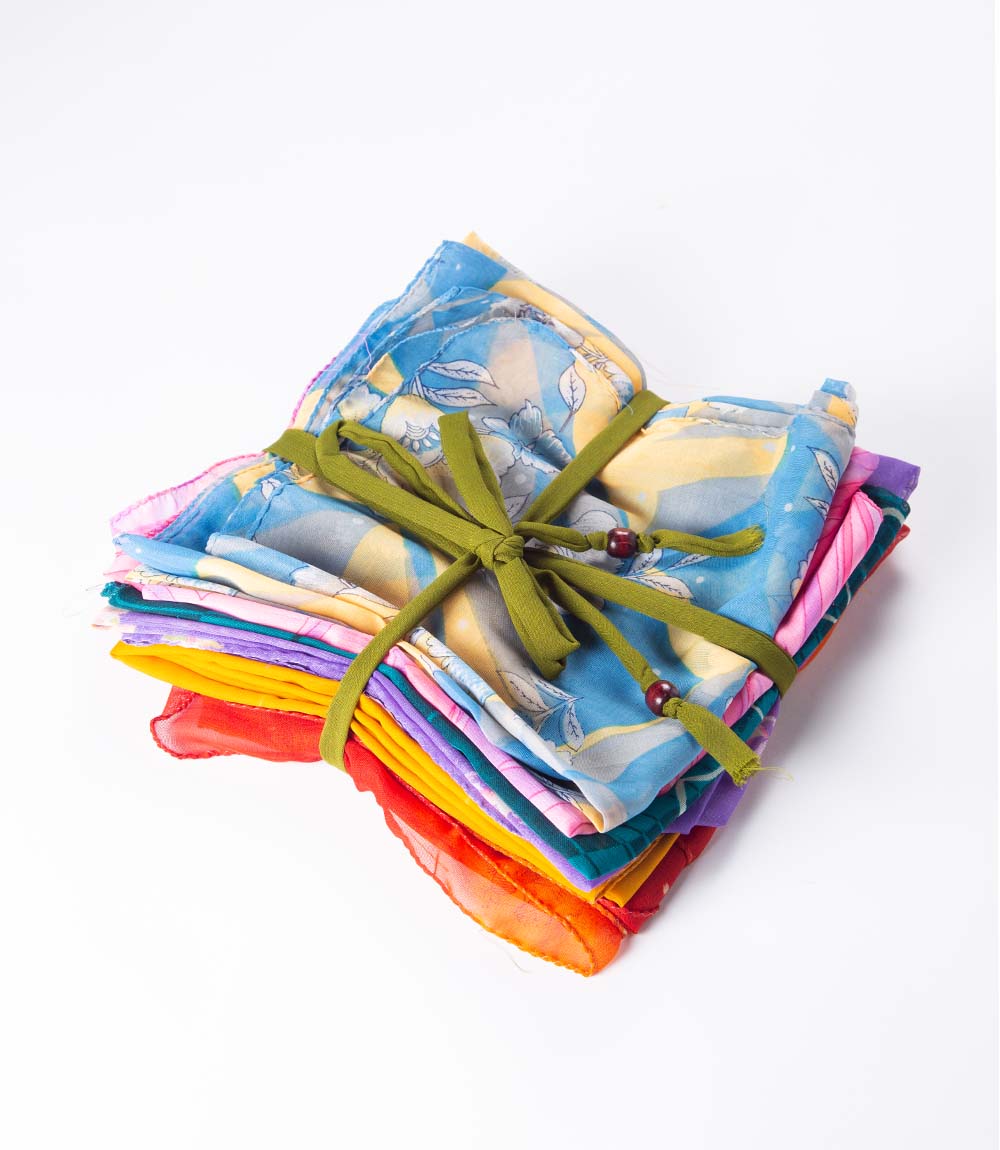 A stack of colorful sari fabric gift wraps tied with a green ribbon on a white background.