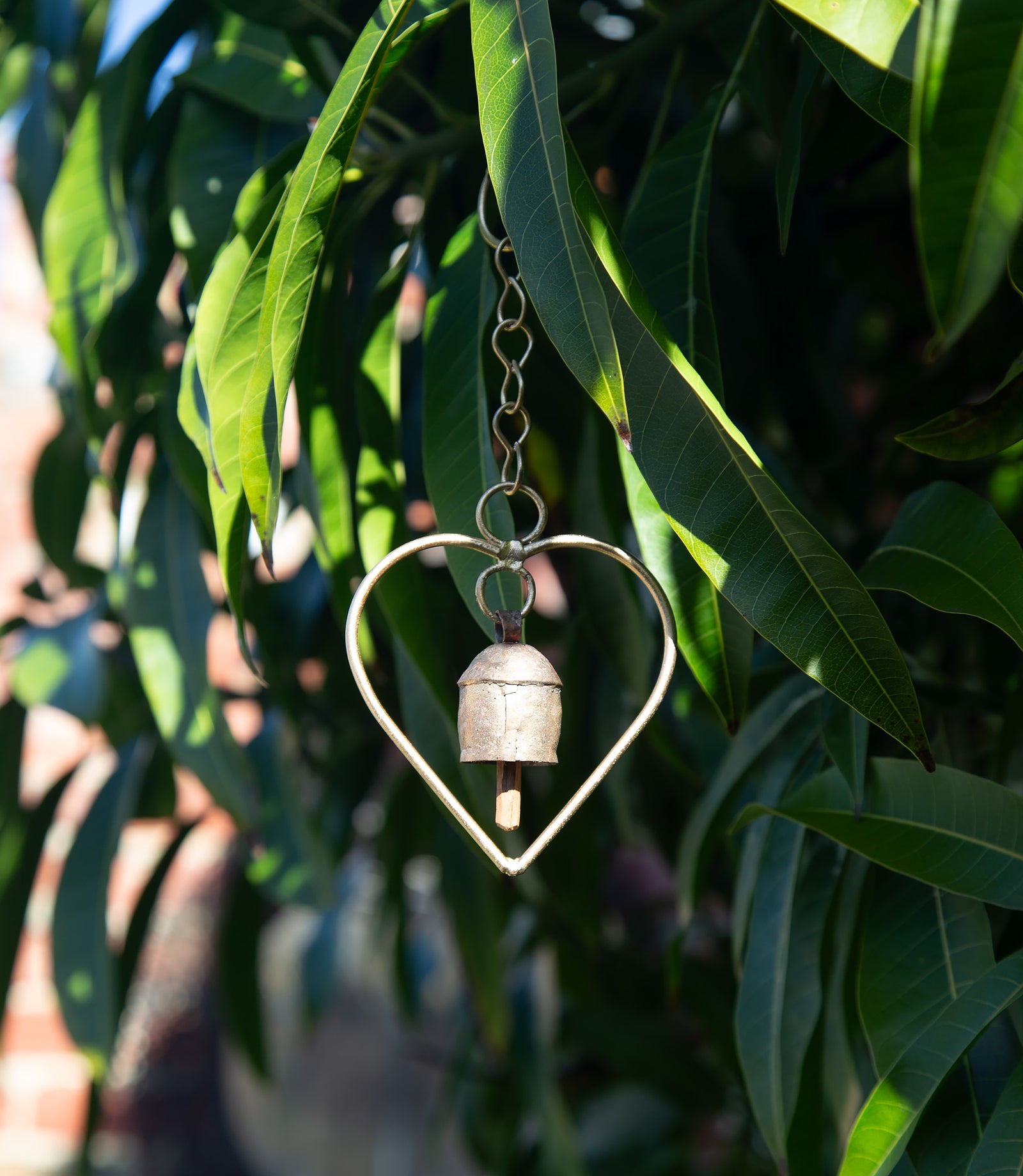 Heart-shaped metal bell hanging among green leaves